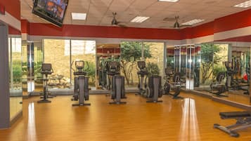 A gym with exercise equipment, large windows, and a television on the wall.