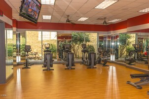 Un gimnasio con equipo de ejercicio, ventanas amplias y un televisor en la pared.
