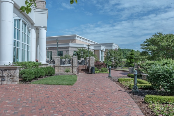 A brick pathway leading to a building with large windows and a landscaped garden.
