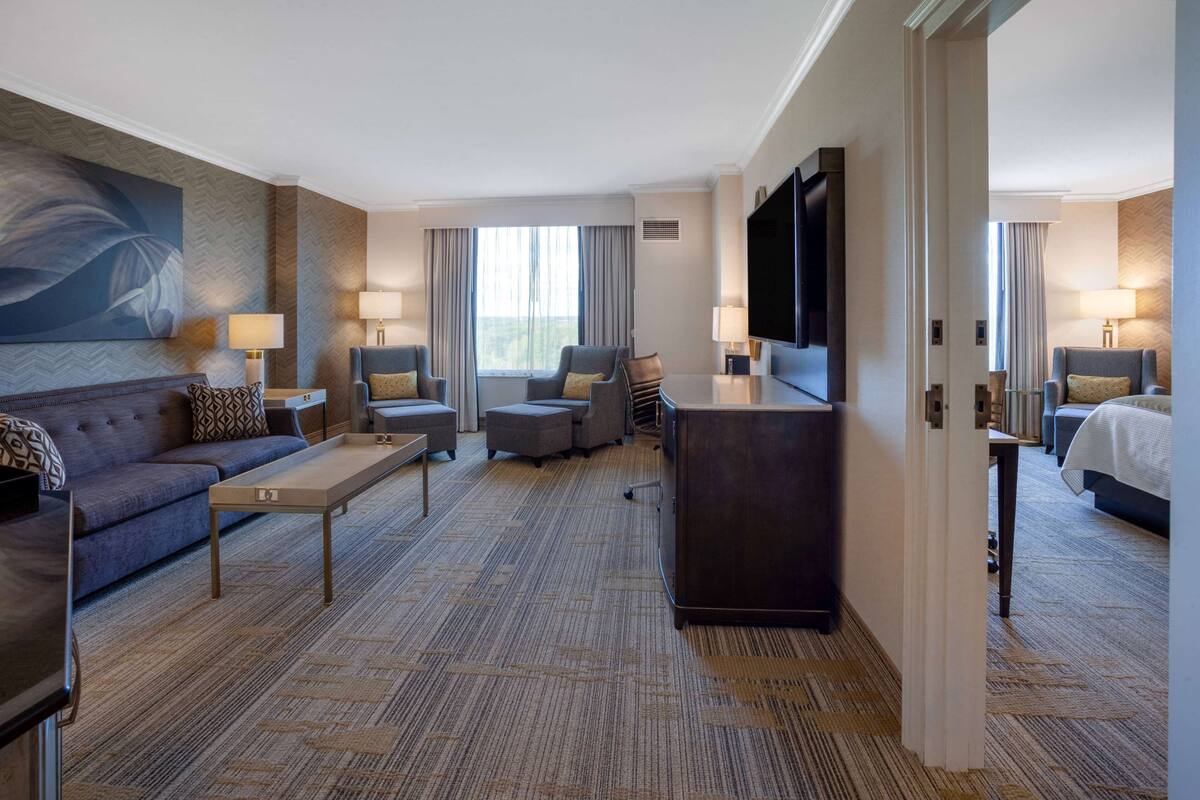 A hotel room with a sofa, two armchairs, a coffee table, a TV, and a desk.