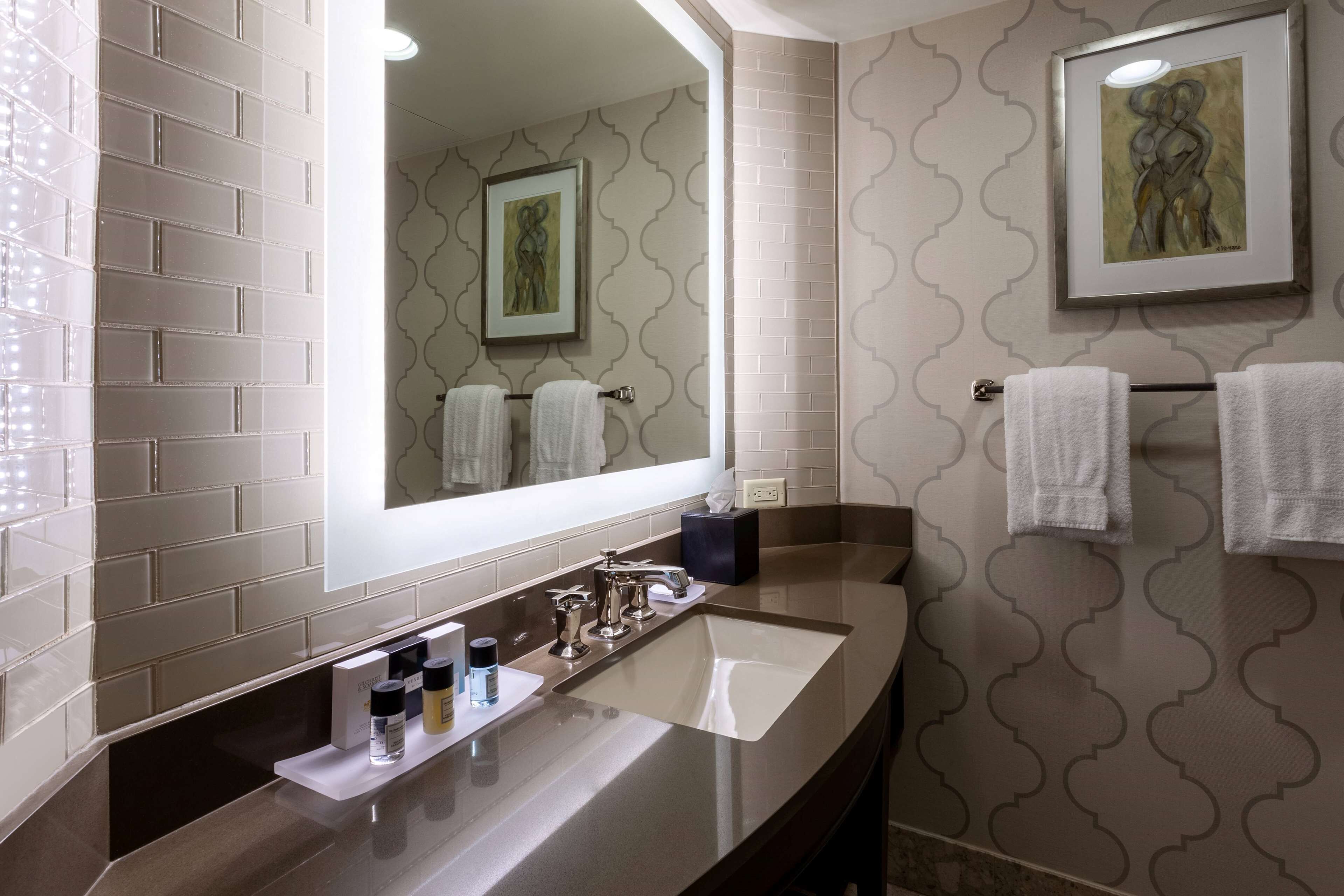 A modern bathroom with a large mirror, a sink, and two towels hanging on a towel rack.