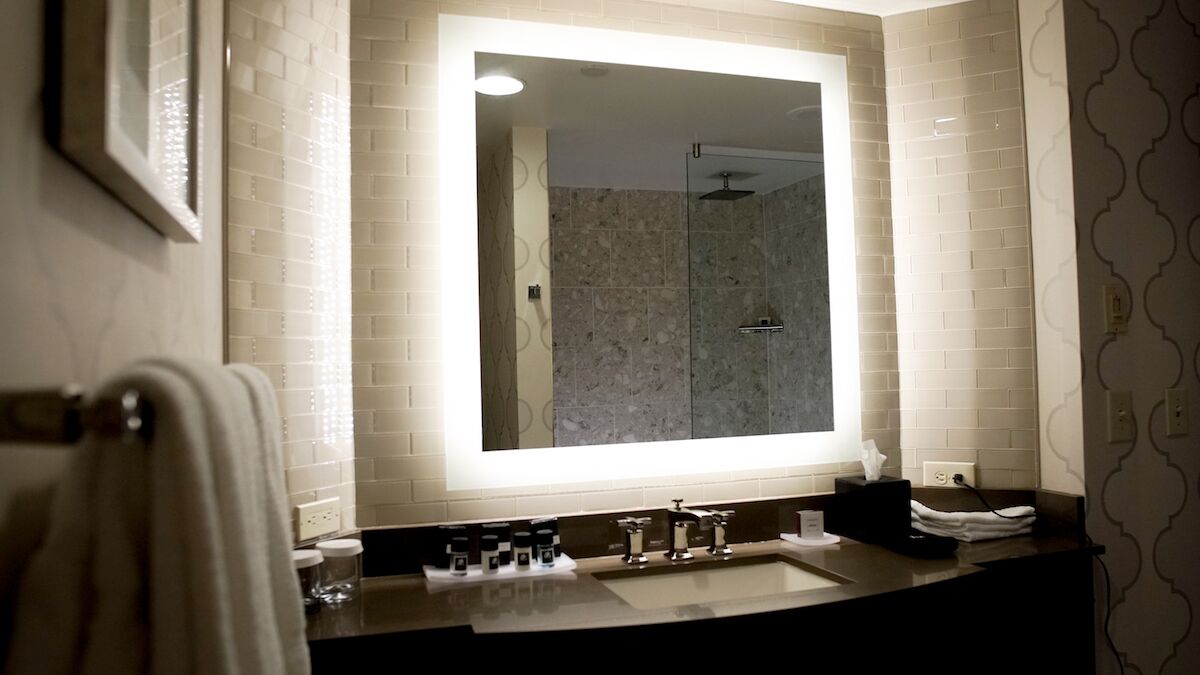 A bathroom with a large mirror, a shower, and a sink with toiletries.