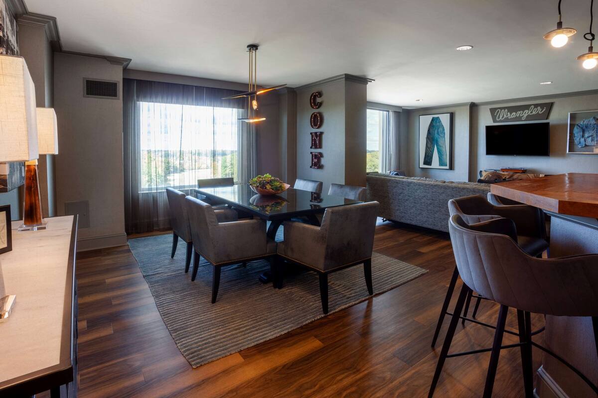 A modern kitchen with a dining area, featuring a large window, a chandelier, and a flat-screen TV.