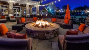 An outdoor seating area with a stone fire pit surrounded by sofas and chairs, string lights overhead, and a building in the background. - Grandover Resort & Spa, a Wyndham Grand Hotel (Greensboro)