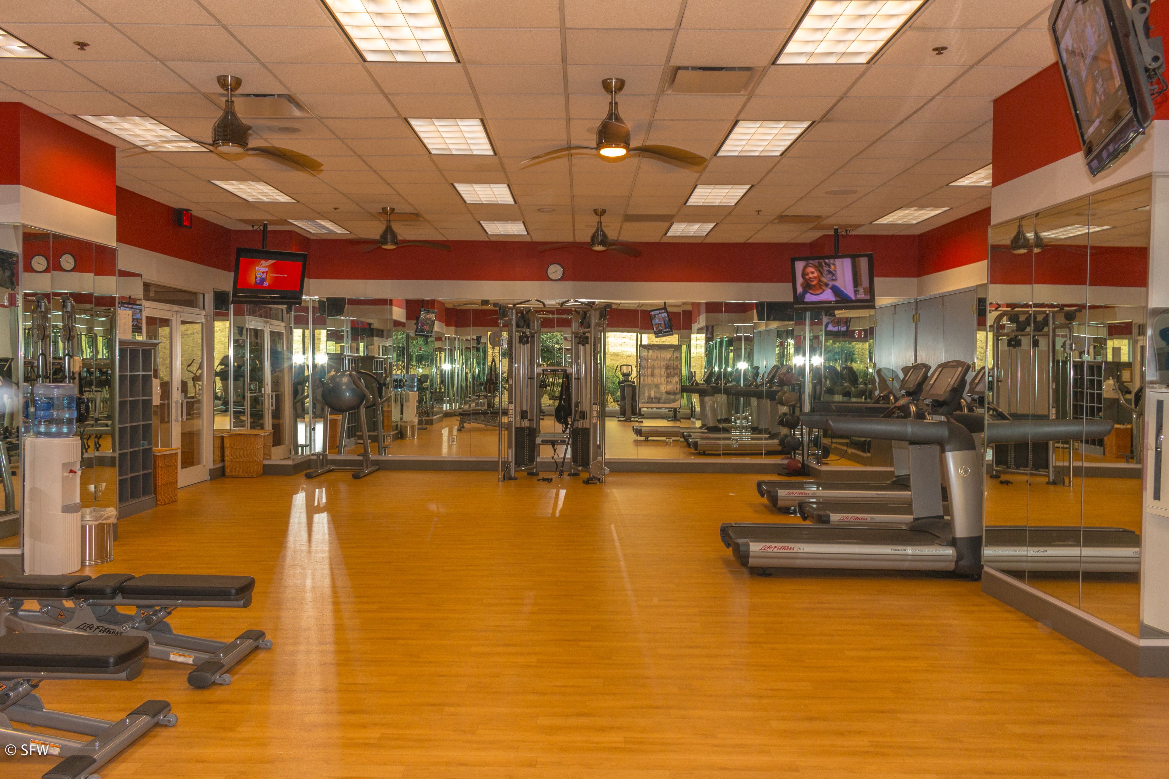A gym with exercise equipment, mirrors, and a television screen.