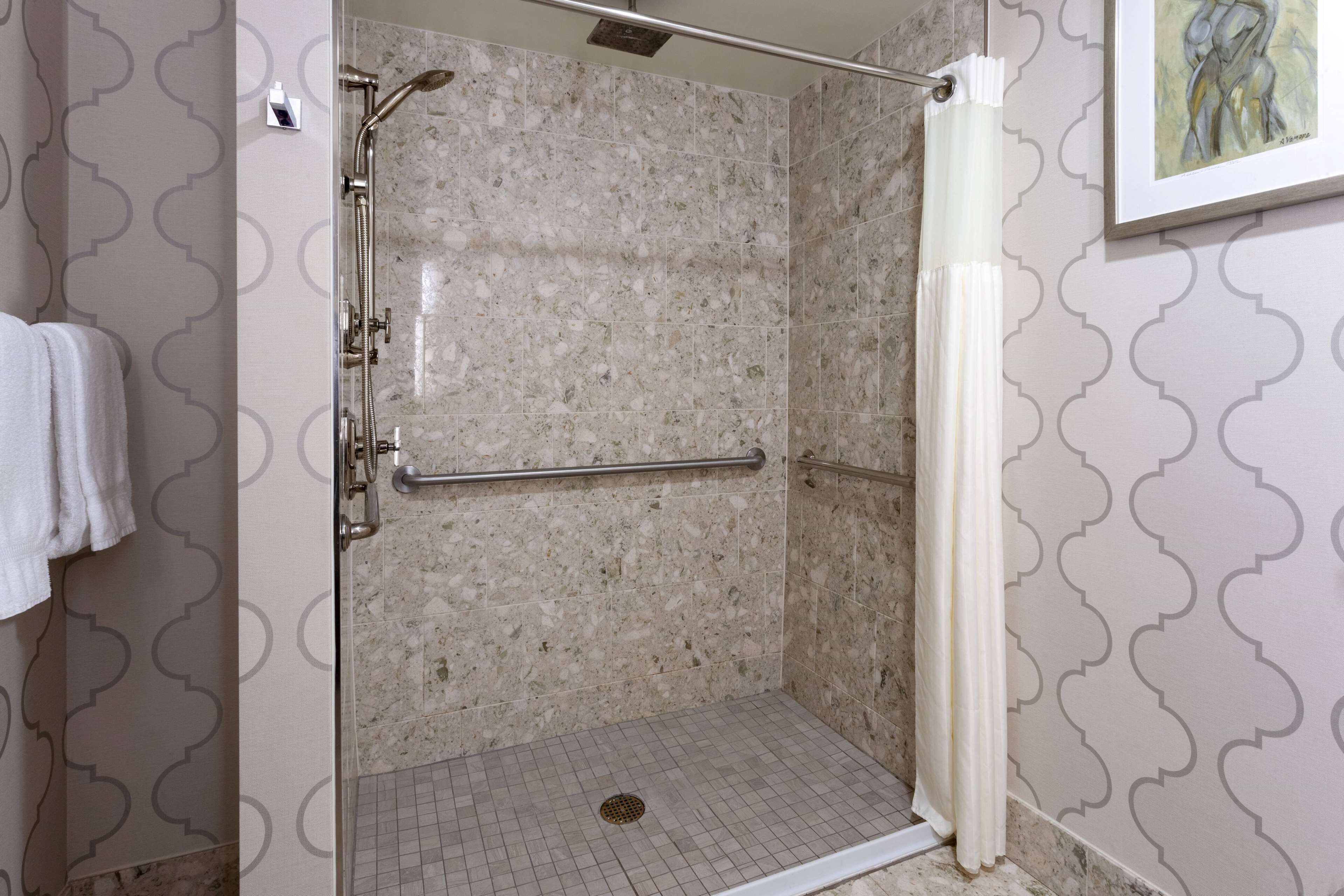 A walk-in shower with a glass door, a handrail, and a showerhead.
