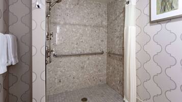A walk-in shower with a glass door, a handrail, and a showerhead.