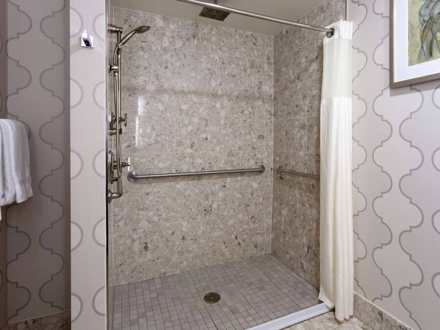 A walk-in shower with a glass door, a handrail, and a showerhead.