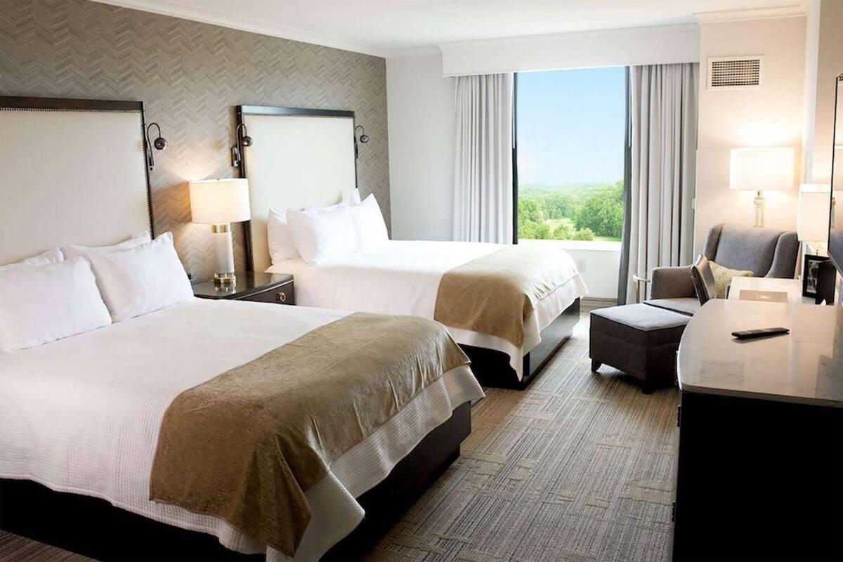 A hotel room with two beds, a desk, and a chair.