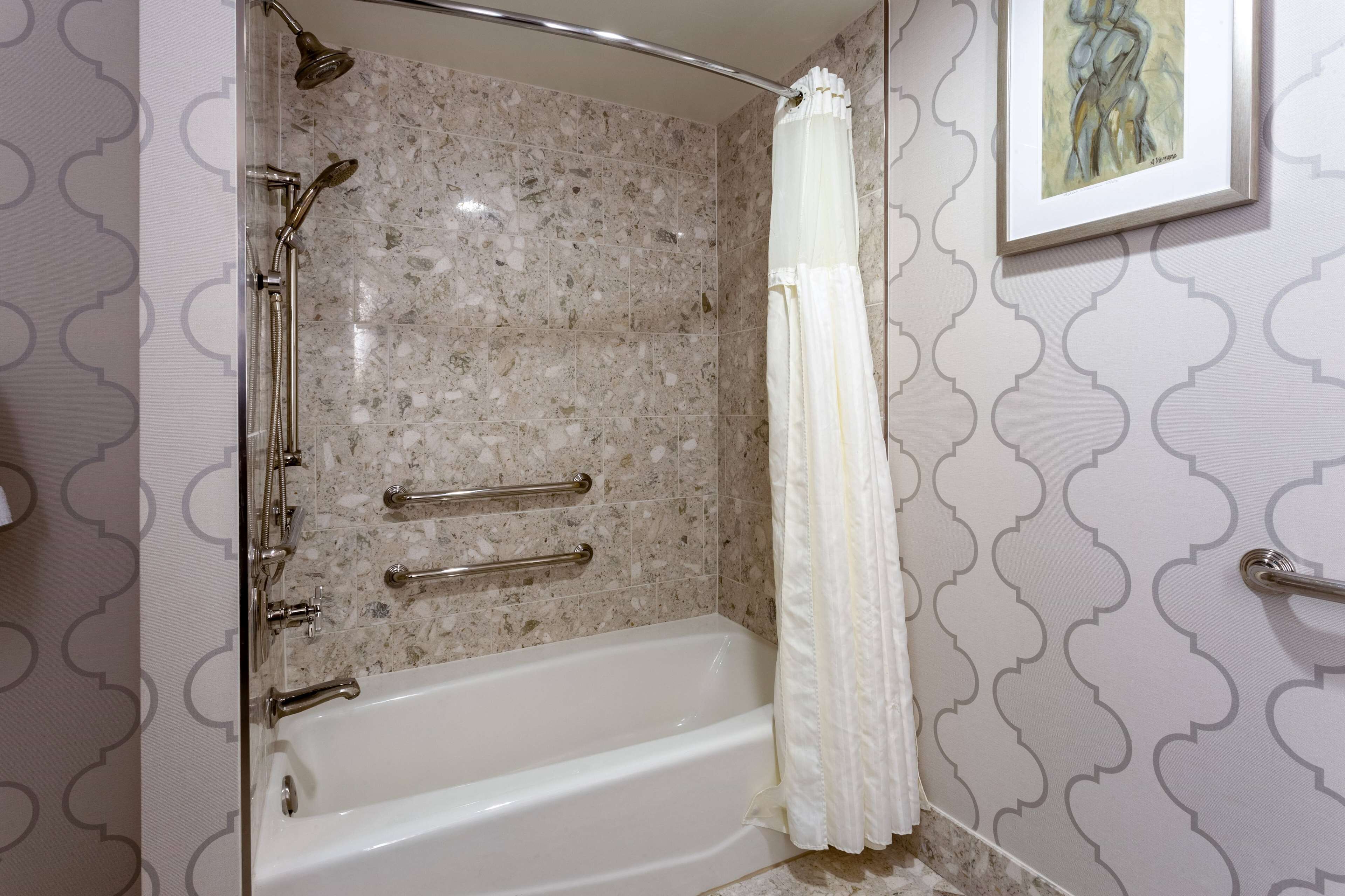 A bathroom with a bathtub, shower, and a handrail.