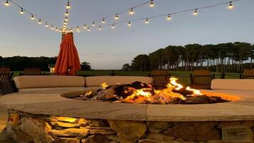 An outdoor seating area with a stone fire pit, string lights, and an orange umbrella.