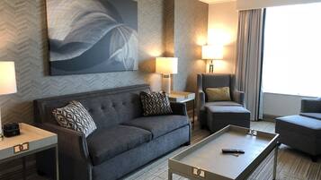 Ein modernes Hotelzimmer mit grauem Sofa, passendem Sessel, einem kleinen Tisch und einem großen, abstrakten Gemälde an der Wand.