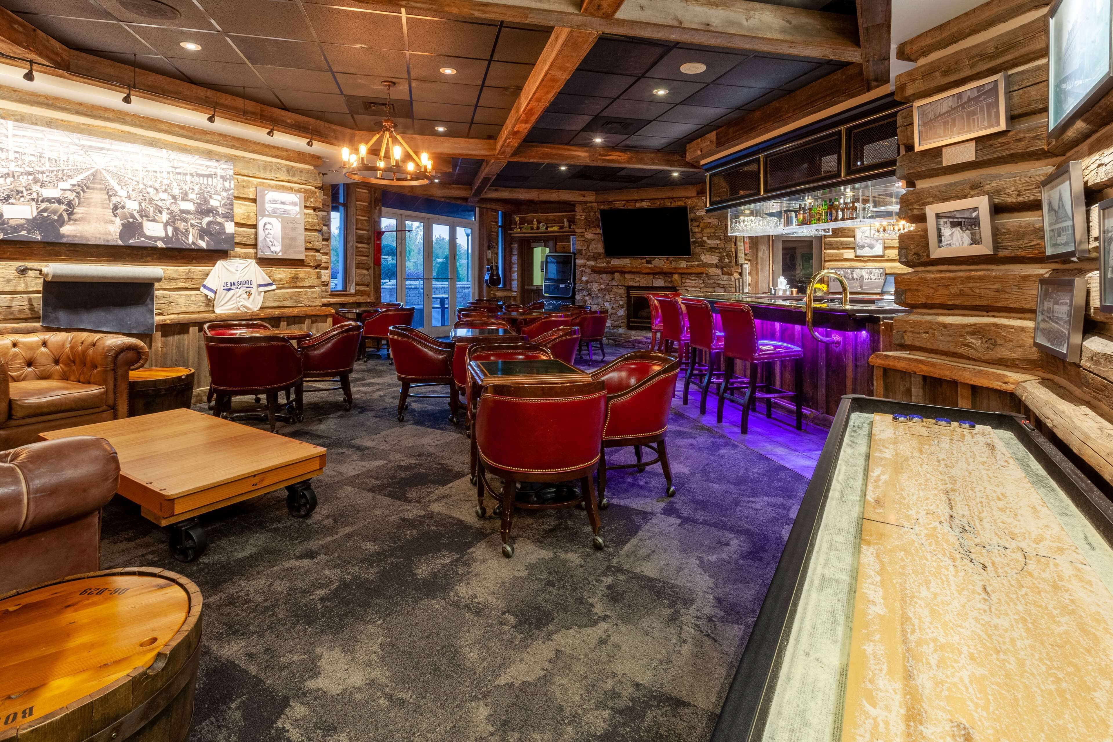 A bar area with wooden walls, red leather chairs, and a bar counter with a television above it.