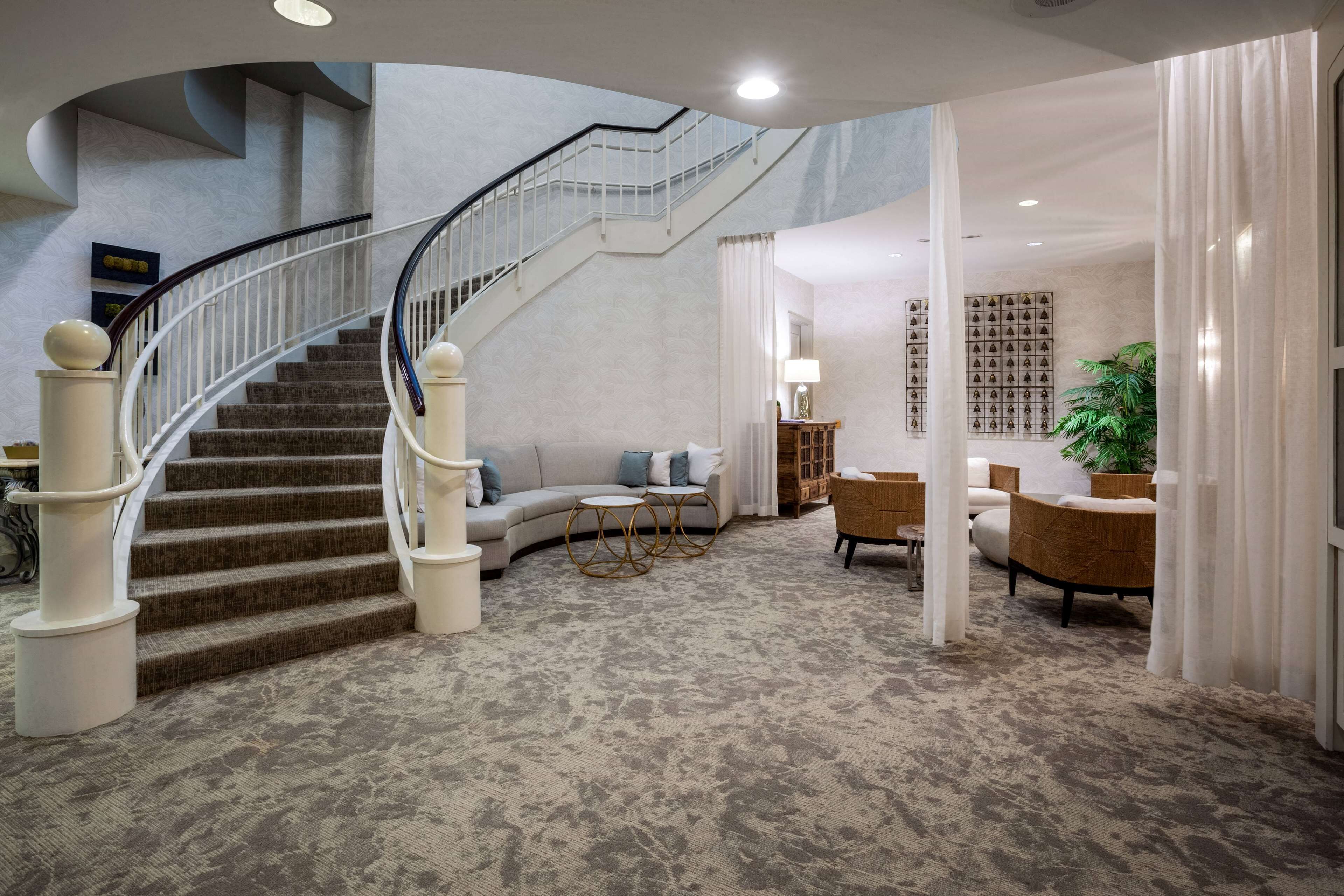 Un hall d’entrée spacieux avec un escalier en colimaçon, un coin salon avec des canapés et une table basse, et un mur décoratif orné de carreaux à motifs.