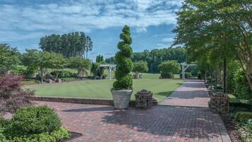 A paved pathway leading to a gazebo, surrounded by lush greenery and a well-maintained lawn.