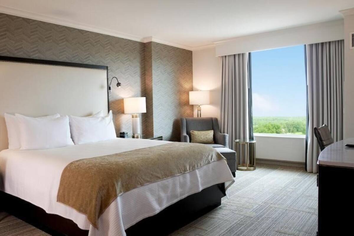 A hotel room with a large bed, two bedside tables with lamps, a chair, a desk, and a view of the outdoors.