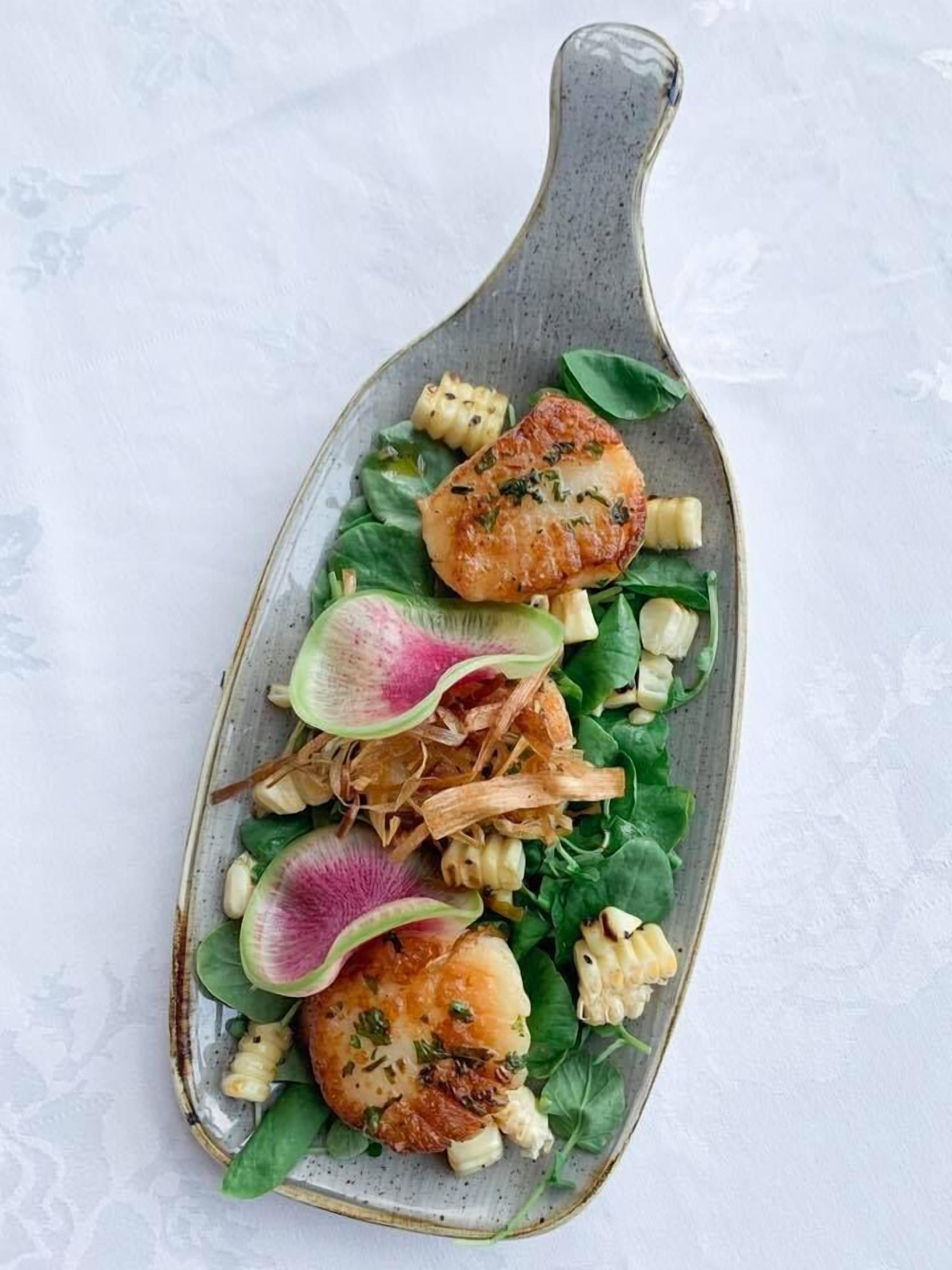 A plate with a variety of food items including scallops, corn, and greens.