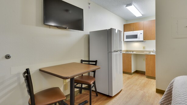 A compact kitchen with a refrigerator, microwave, and a small dining area with a table and two chairs. - HomeTowne Studios by Red Roof Austin (Austin)