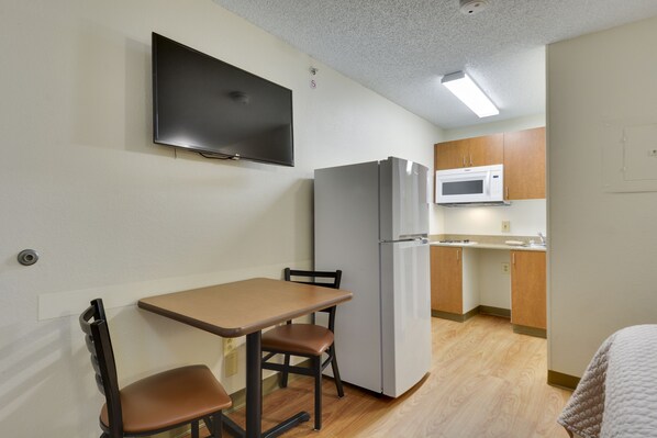 A compact kitchen with a refrigerator, microwave, and a small dining area with a table and two chairs. - HomeTowne Studios by Red Roof Austin (Austin)