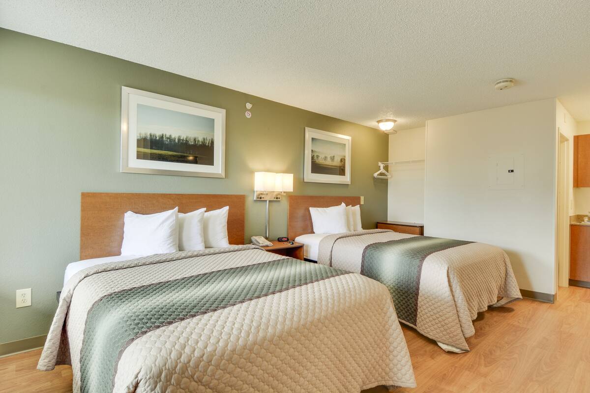 A hotel room with two beds, a nightstand, a lamp, and two framed pictures on the wall.