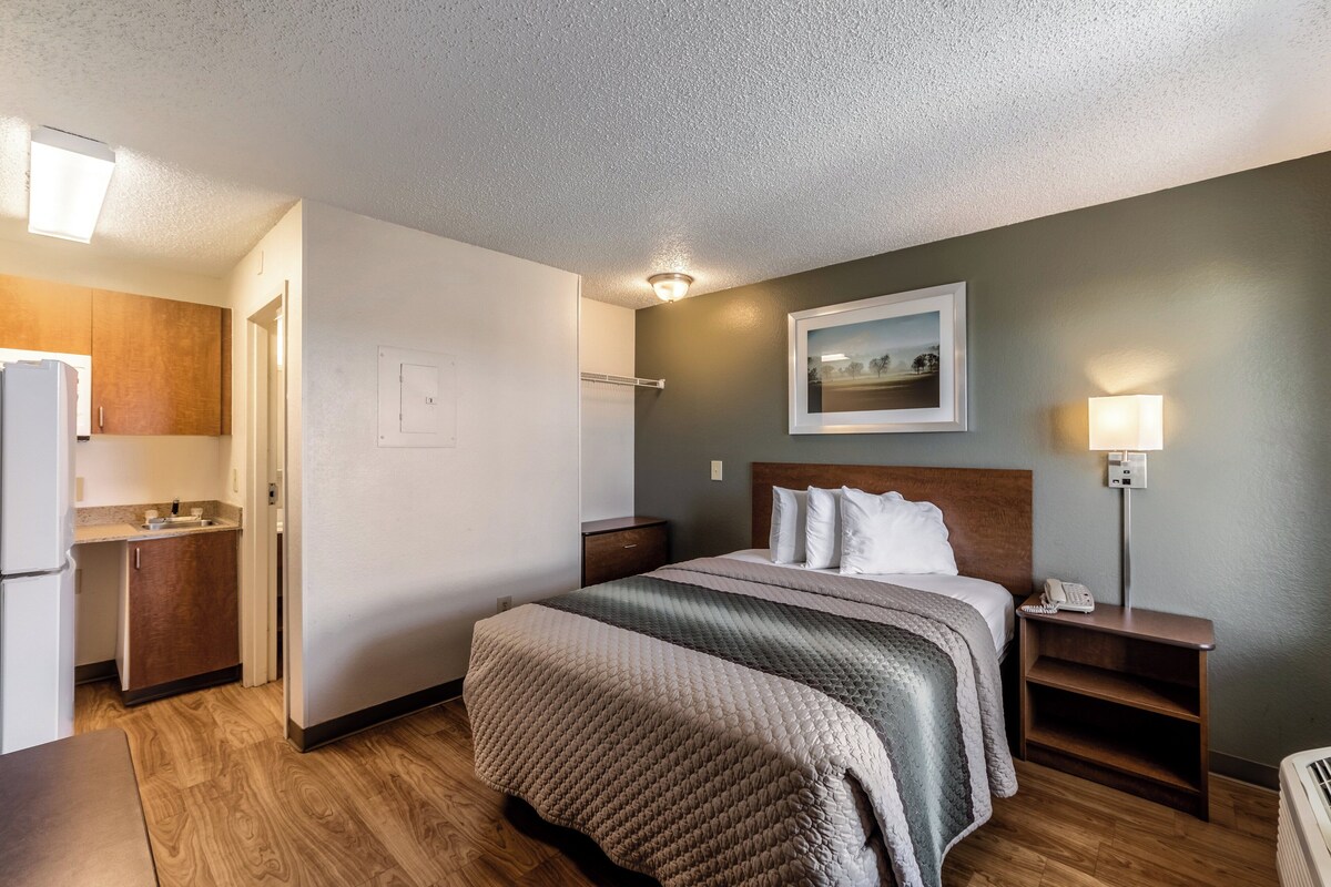 A hotel room with a bed, bedside table, lamp, and a view of the cityscape.