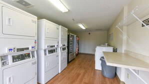 A laundry room with multiple washing machines and dryers, a trash bin, and a countertop.