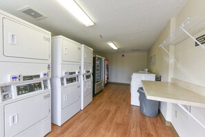 A laundry room with multiple washing machines and dryers, a trash bin, and a countertop.