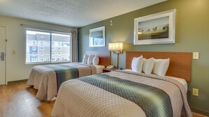 A hotel room with two beds, a large window, a painting on the wall, and a lamp. - HomeTowne Studios by Red Roof Austin (Austin)
