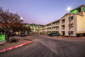 A motel with multiple floors, a green sign indicating the entrance, and a fire lane marked on the pavement. - HomeTowne Studios by Red Roof Austin (Austin)