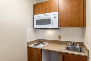 A compact kitchen with a built-in microwave, a stainless steel sink, and wooden cabinets. - HomeTowne Studios by Red Roof Austin (Austin)