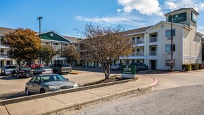 A hotel with a green entrance sign, multiple floors, and a parking lot with cars.