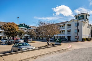 A hotel with a green entrance sign, multiple floors, and a parking lot with cars.
