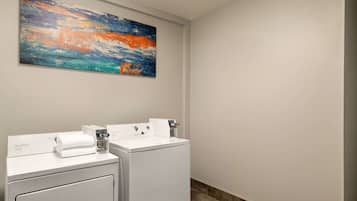 Un baño de hotel con dos lavamanos blancos, un cuadro abstracto grande sobre los lavamanos y suelo de baldosas.
