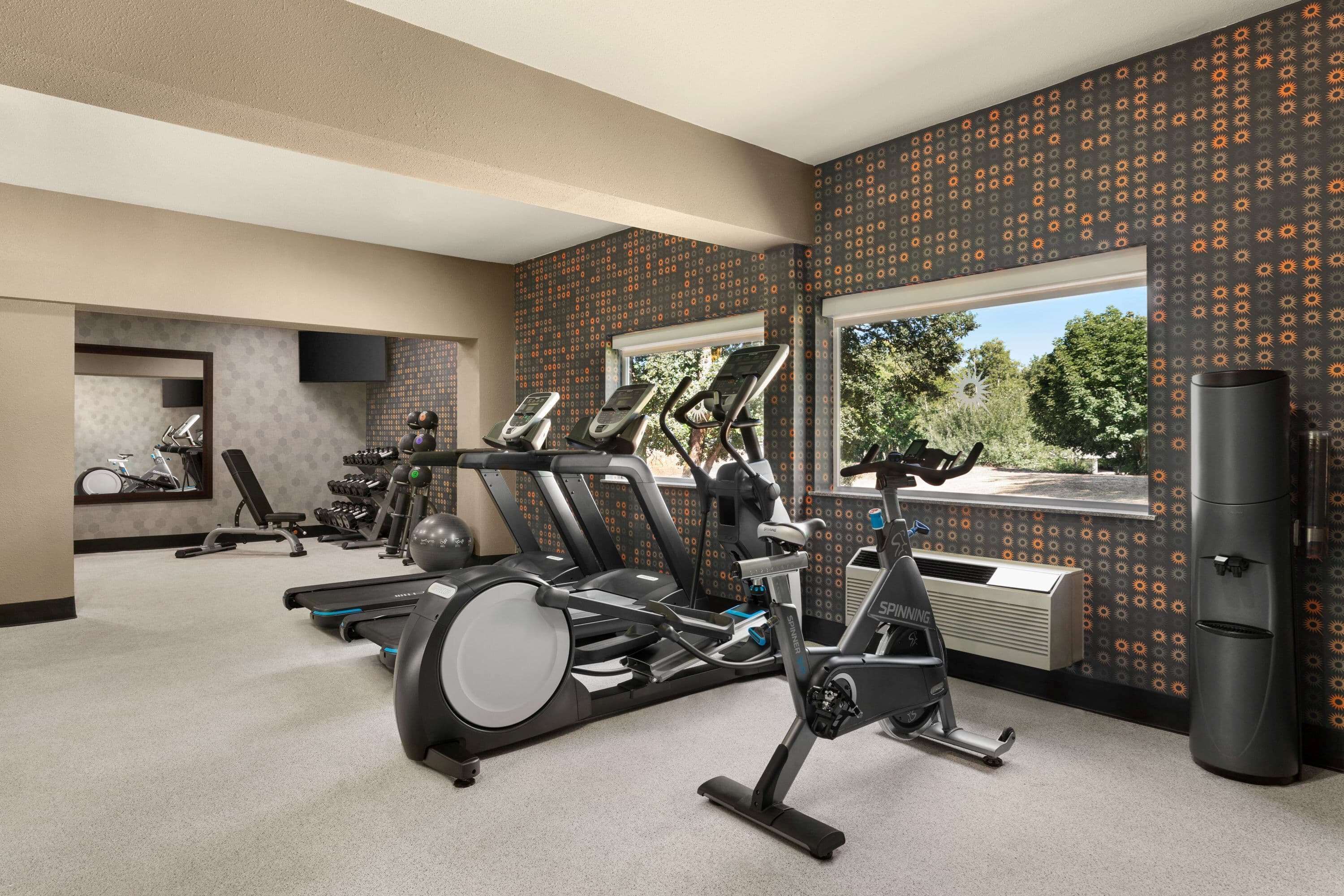 A gym with multiple exercise machines, a large window, and a view of trees.