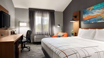 A hotel room with a bed, desk, chair, TV, and artwork on the wall.