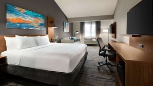 A hotel room with a large bed, a desk, a chair, a TV, and a painting on the wall. - La Quinta Inn & Suites by Wyndham Salem OR (Salem)