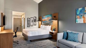 A modern hotel room with a large bed, a desk, a sofa, and artwork on the walls.