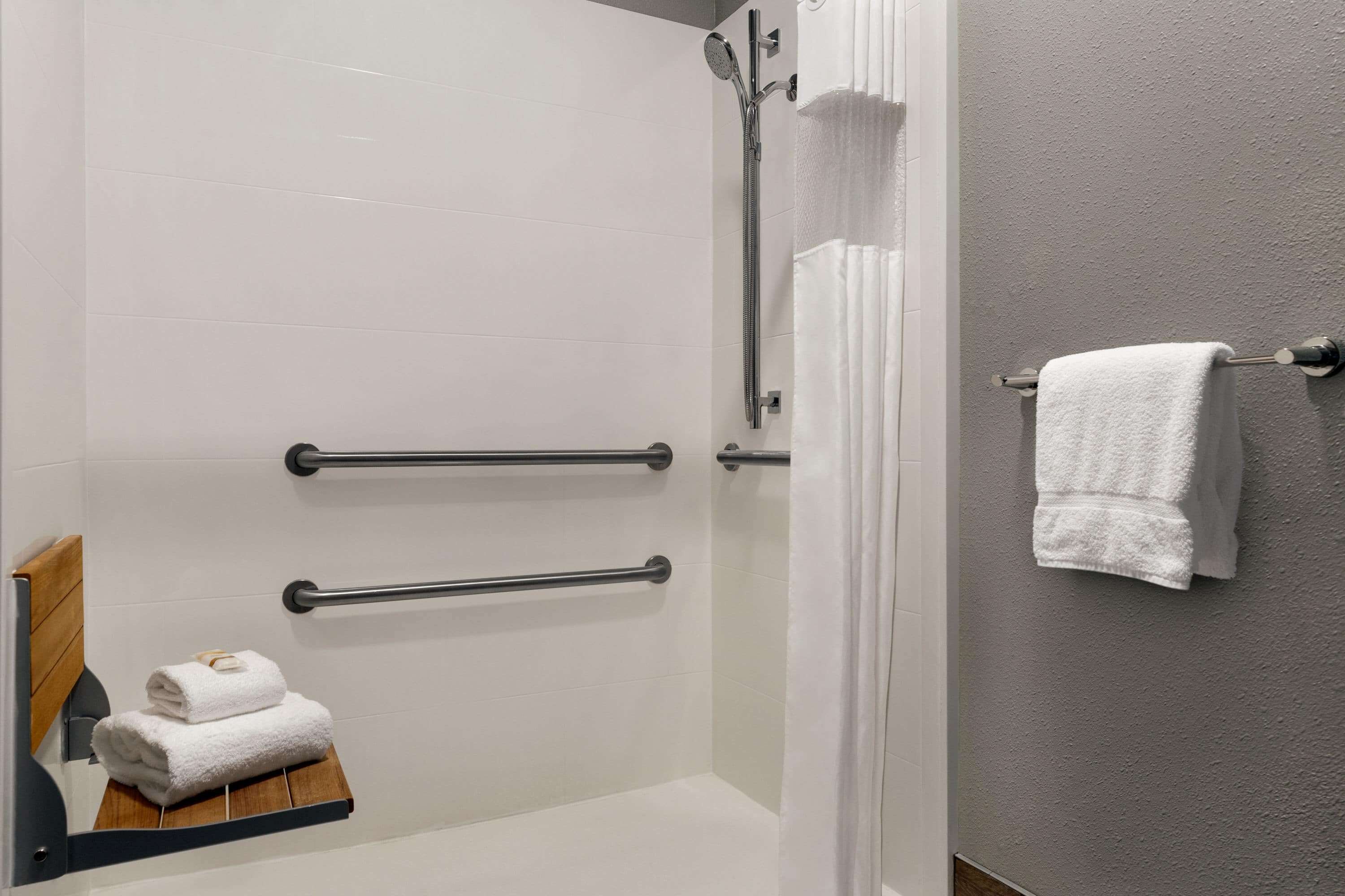A modern bathroom with a glass shower enclosure, white tiles, and a wooden bench with towels.