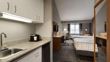Quarto de hotel com cozinha compacta, cama, escrivaninha e um espelho grande.