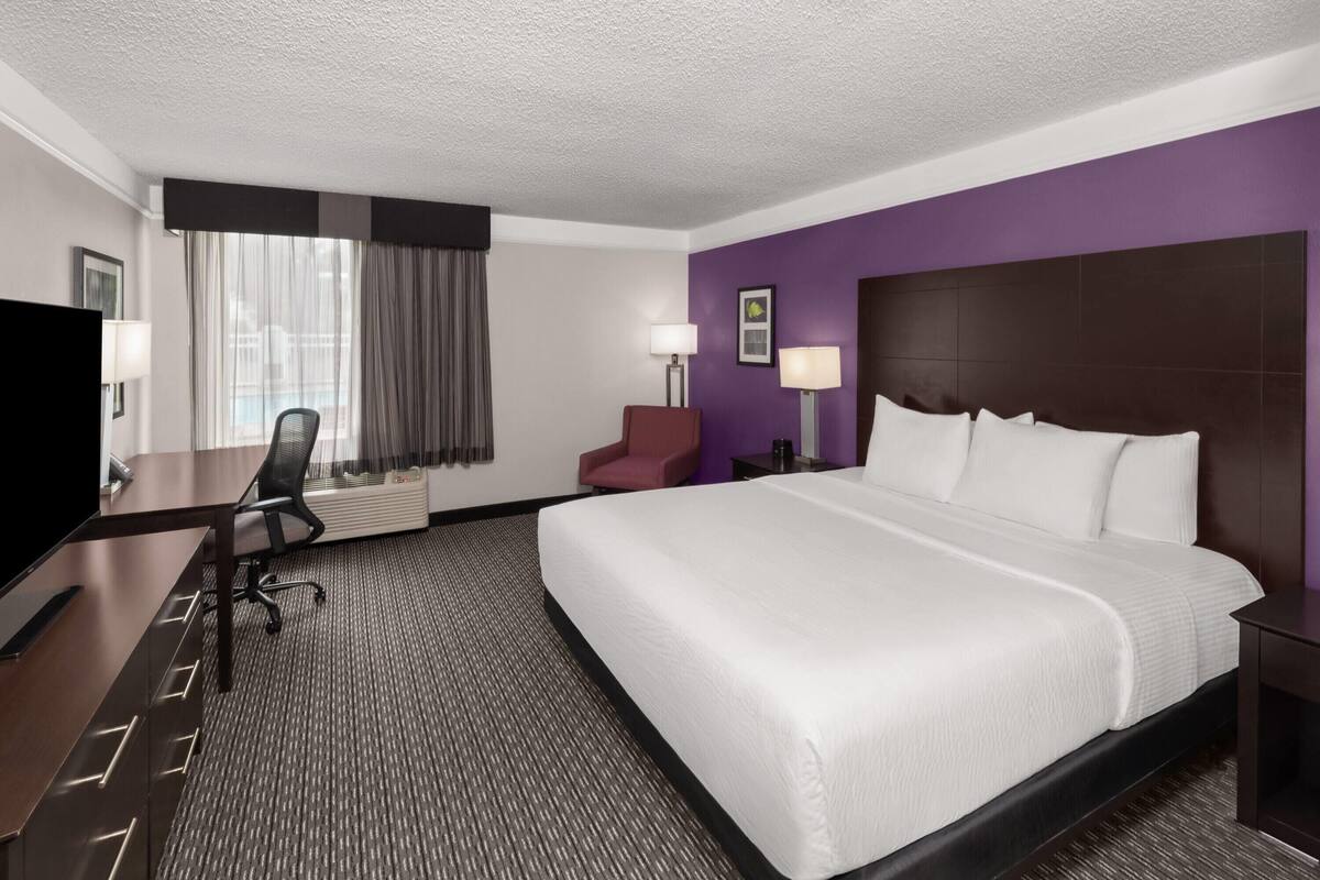 A hotel room with a large bed, a desk with a chair, a TV, and a window with curtains.