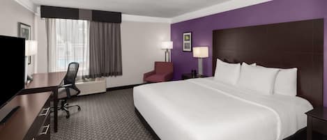 Habitación de hotel con una cama grande, un escritorio con silla, un televisor y una ventana con cortinas.
