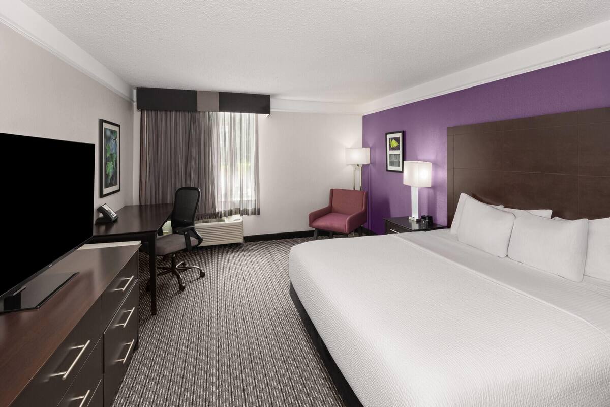A hotel room with a bed, a desk, a chair, a TV, and a lamp.