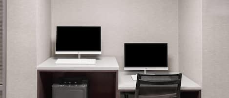 Un espacio de oficina pequeño y cerrado, con dos escritorios, cada uno con monitor de computadora, teclado y silla.