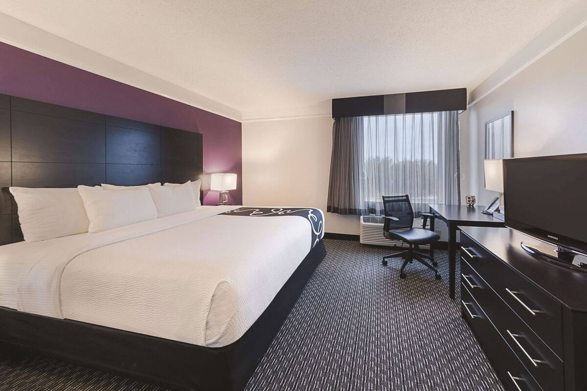 A hotel room with a large bed, a desk with a chair, a TV, and a window with curtains.