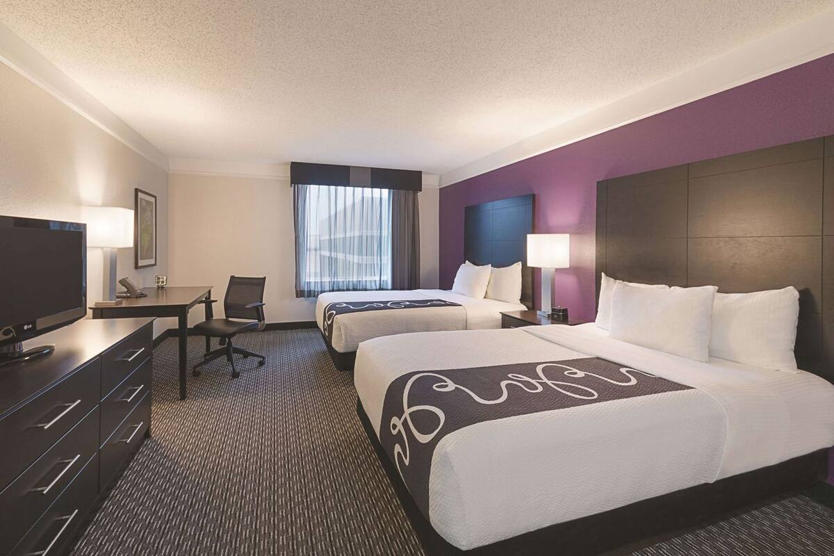 A hotel room with two beds, a desk, a TV, and a window with curtains.