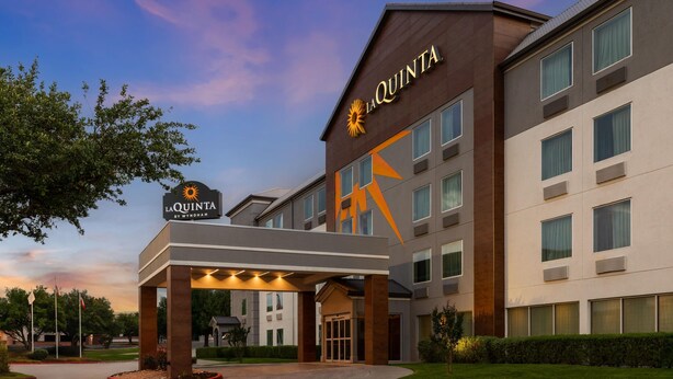 Ein Hotel mit einem gut sichtbaren 'La Quinta by Wyndham'-Schild, einem überdachten Eingang und einer modernen Fassade.