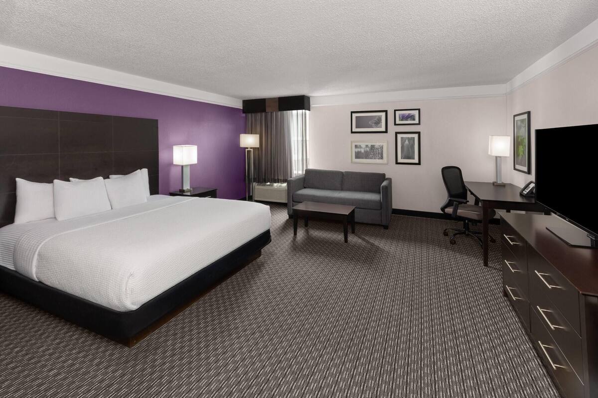 A hotel room with a large bed, a sofa, a desk, and a television.