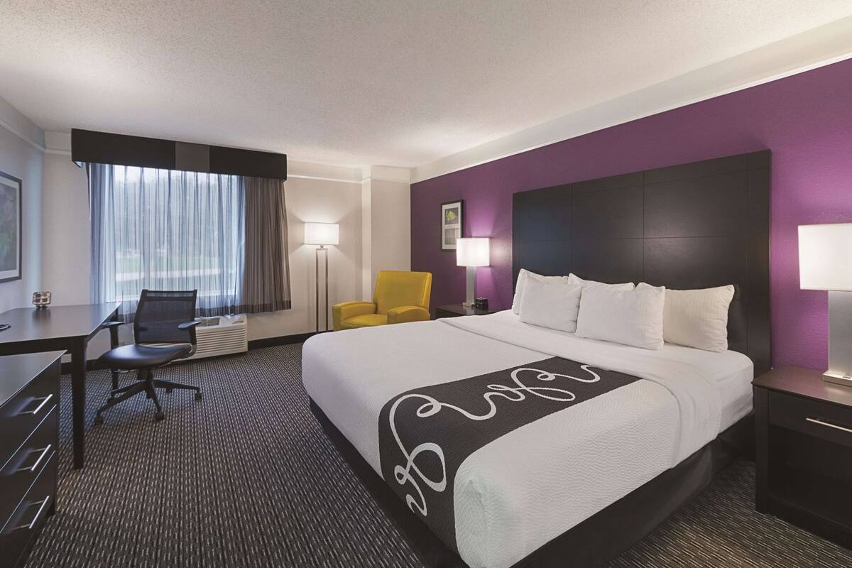A hotel room with a bed, a desk, a chair, and a nightstand.