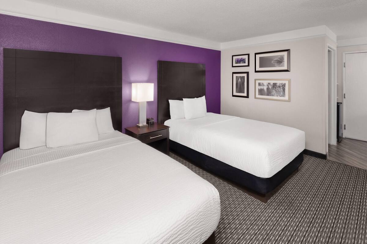 A hotel room with two beds, a nightstand, a lamp, and framed pictures on the wall.