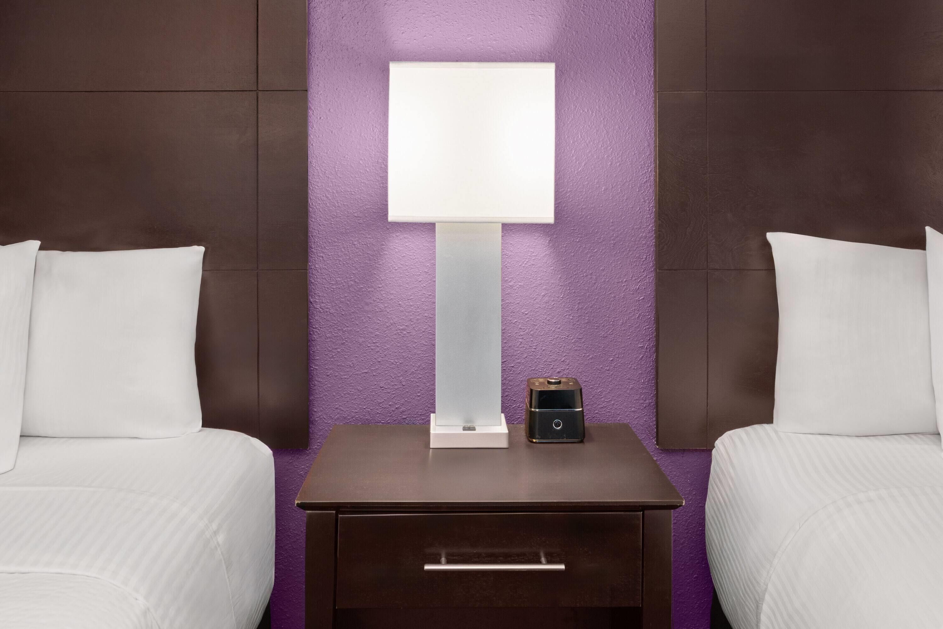 Ein Hotelzimmer mit zwei Betten, einem Nachttisch mit Lampe, einem kleinen Tisch und einer Schublade.